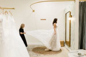 beautiful bride looking in the mirror while her bridal stylist fixes the train of her dress