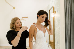 woman standing behind a bride in a wedding dress helping her adjust her straps