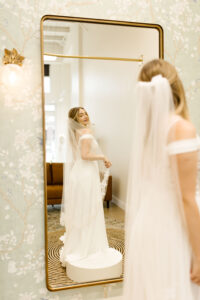 woman standing in a wedding dress and admiring herself in a mirror