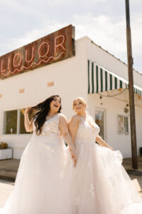 2 women standing outside in wedding dresses, smiling