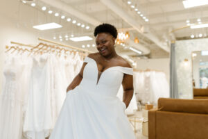 Happy plus size bride in front of racks of wedding gowns in Ivoryology bridal store in Cordova TN