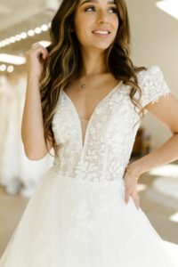 Woman smiling showing off the bodice of a cap sleeve wedding dress