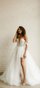 A bride modeling a white off the shoulder wedding dress with a tulle skirt.