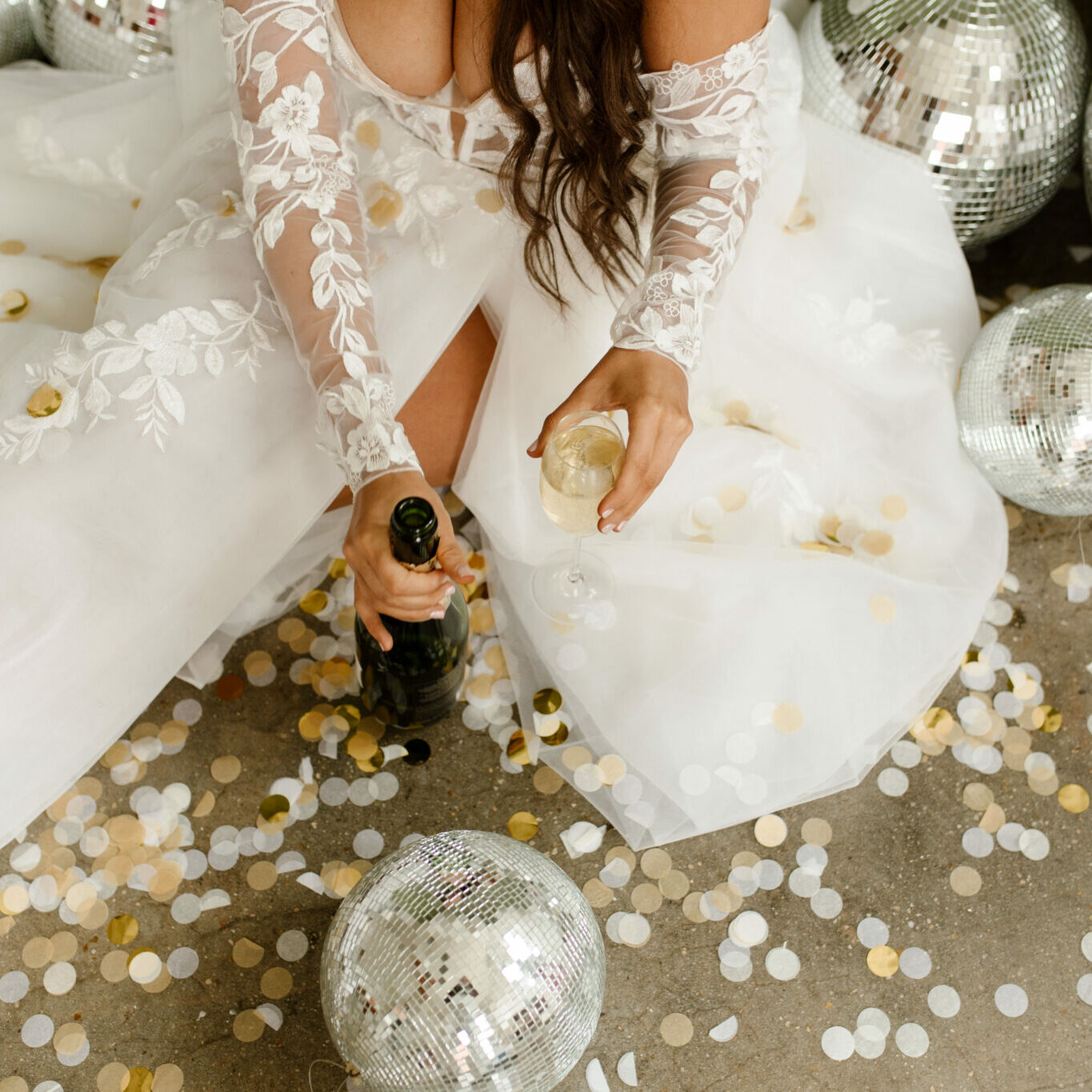 A bride pouring some champagne while wearing a lace sleeve wedding dress.