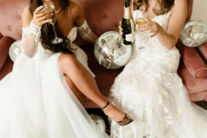 Two brides to be sitting on a couch and drinking champagne.